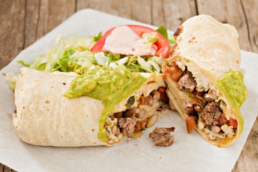 Burrito de carne servido con guacamole por encima y acompañado con ensalada.