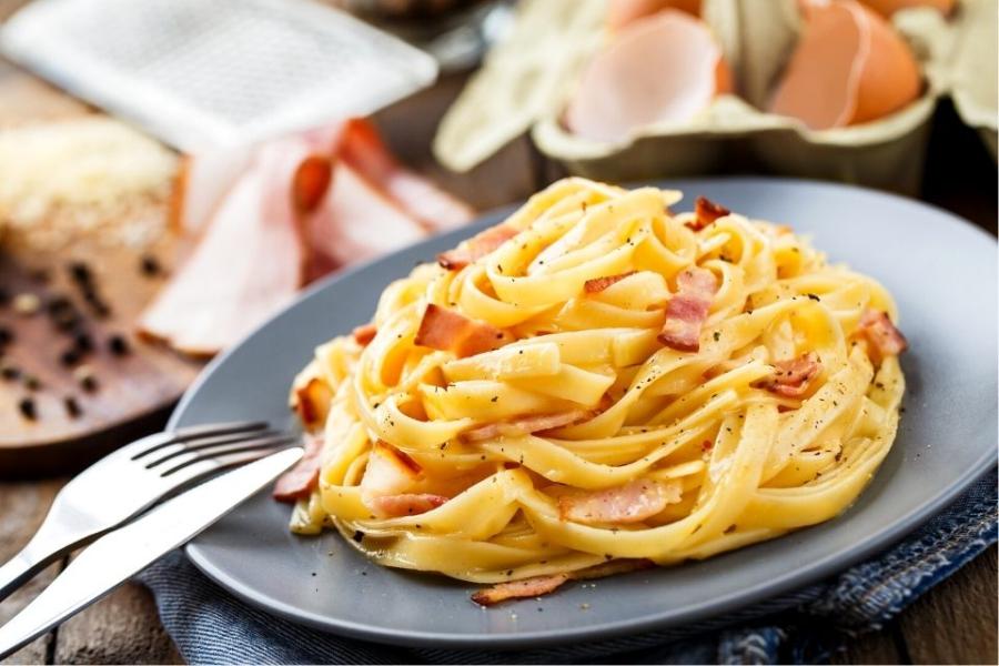 Un plato de cintas a la carbonara con algunos de los ingredientes al fondo.