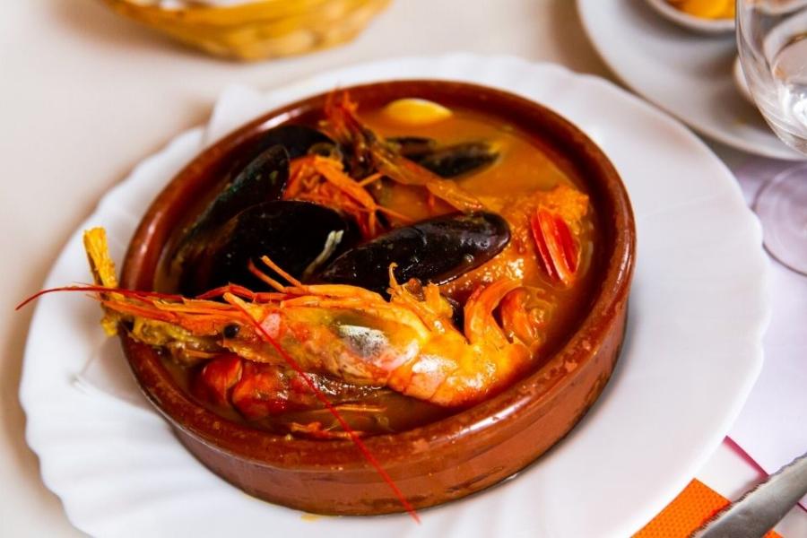 Suquet de pescado con langostinos y mejillones servido en una cazuela de barro.