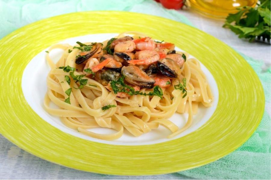 Cintas con marisco presentada en un plato de loza con borde de color verde pálido.