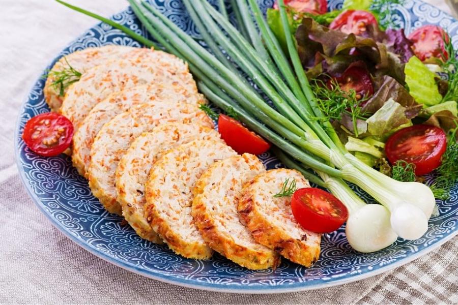 Un plato con rodajas de rollo de pollo, ensalada y cebolletas.