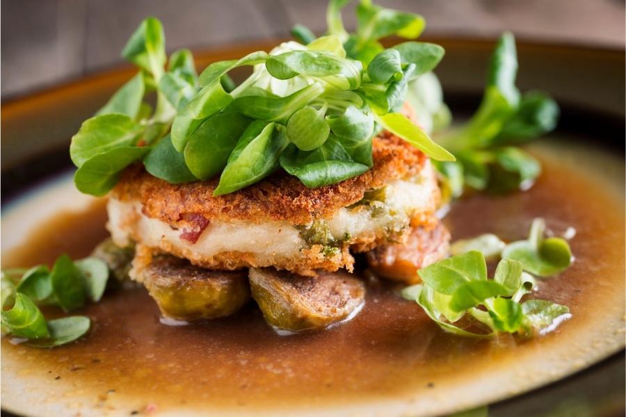 Un plato con tortitas de patata sobre coles de bruselas y salsa, decoradas con canónigos.