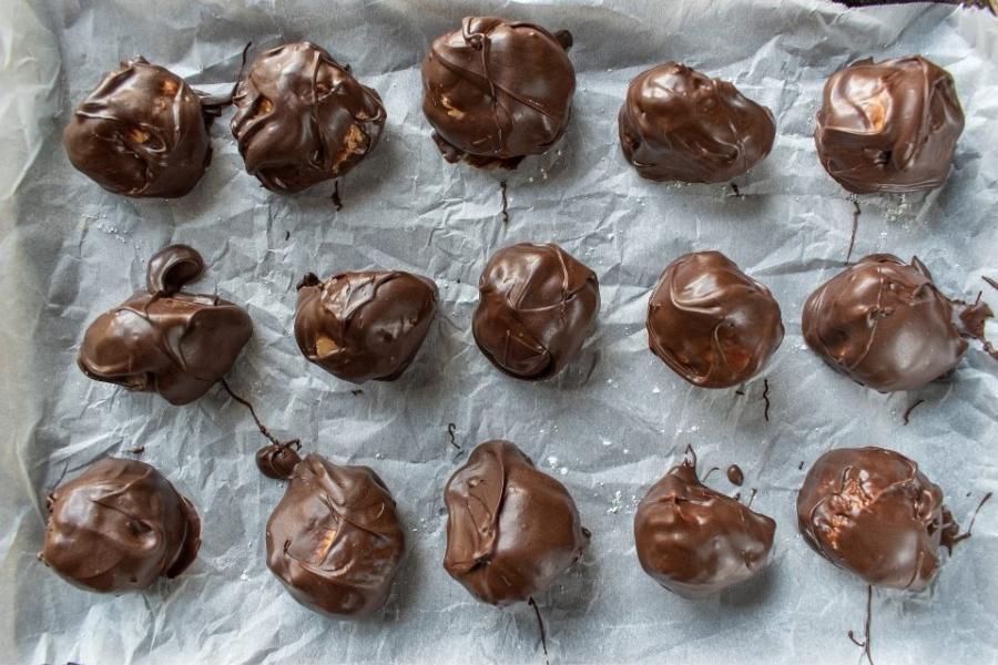 Bolas de mantequilla de cacahuete y chocolate secándose sobre papel parafinado.