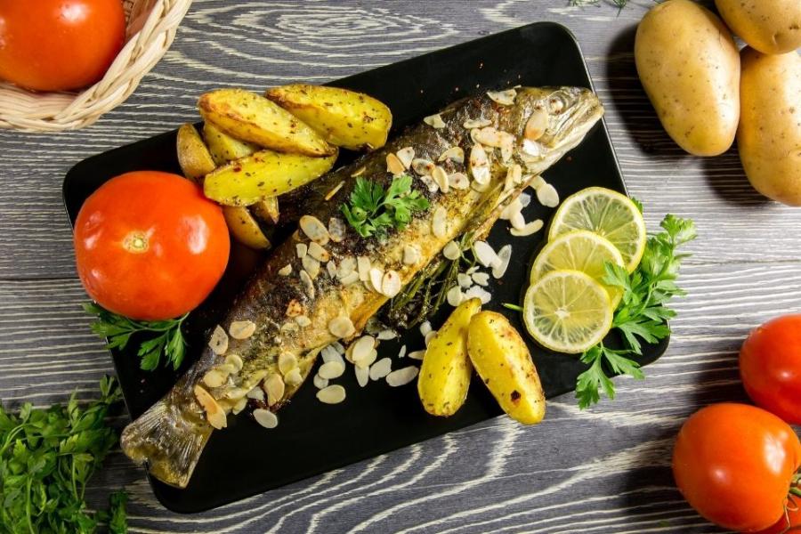 Trucha con almendras acompañada de patatas, rodajas de limón y un tomate.