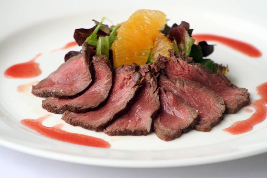 Canguro a la plancha fileteado fino con salsa de frambuesa y ensalada de naranja.
