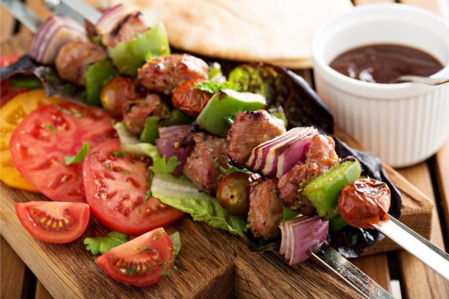 Pinchos de ternera acompañados de rodajas de tomate, salsa y pan plano.