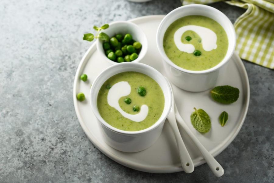 Dos tazas con porciones individuales de sopa de guisantes decorada con nata líquida y menta.