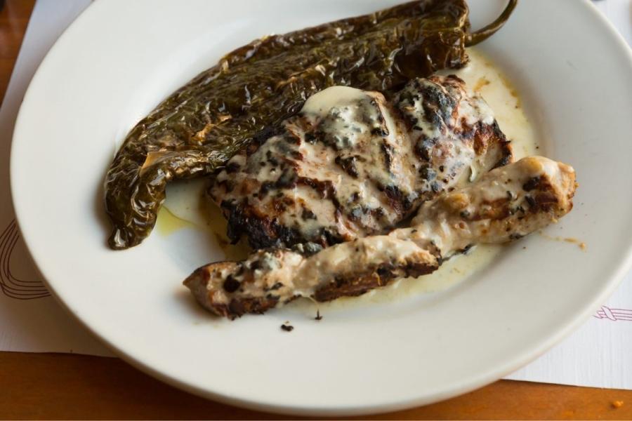 Un plato con cerdo ibérico frito cubierto con salsa roquefort y un pimiento asado a su lado.