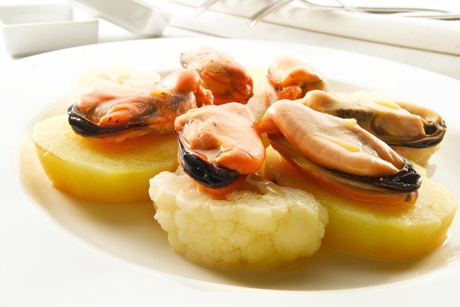 Mejillones con patatas en un plato, las patatas peladas, los mejillones sin valvas.