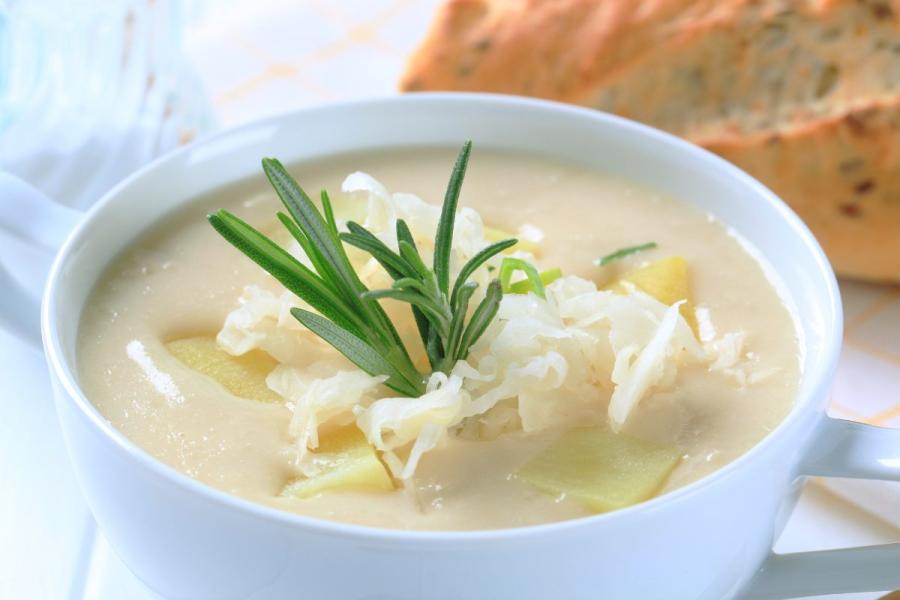 Una taza con sopa de coliflor decorada con romero y queso rallado.