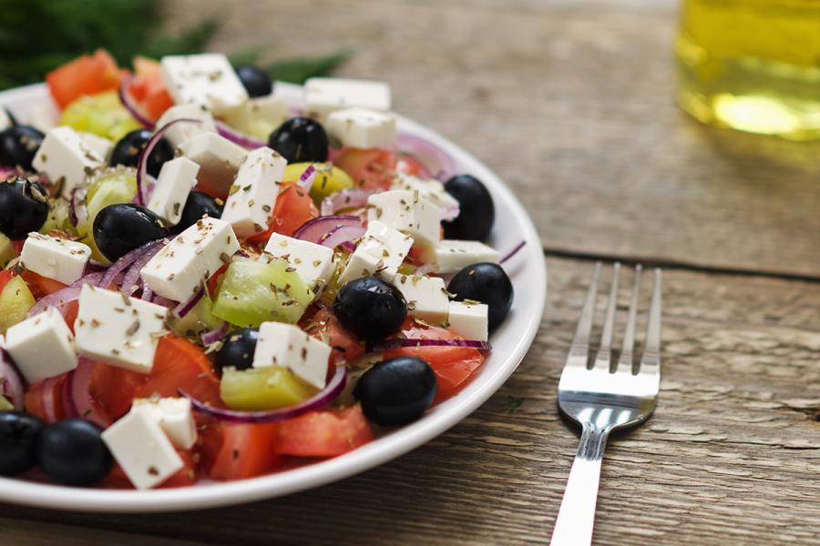 Ensalda griega con tomate, queso feta, pepino, cebolla y aceitunas negras en un plato.
