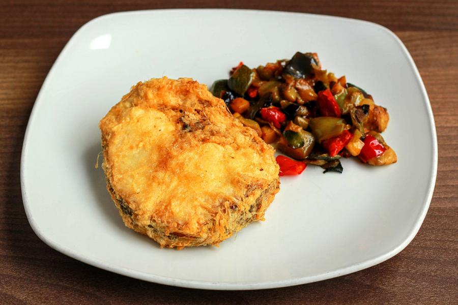 Una rodaja de merluza rebozada a la romana acompañada de verduras braseadas.