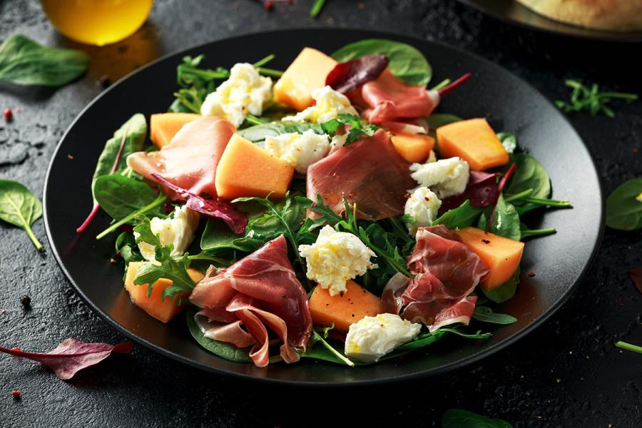Un plato con ensalada de melón con jamón de Parma y queso mozzarella.