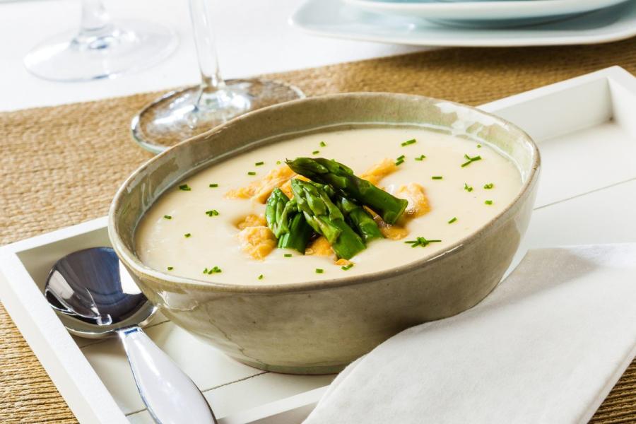 Un cuenco con crema de espárragos decorada con cuscurros de pan, puntas de espárragos y perejil picado.
