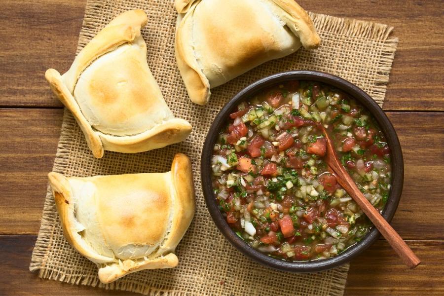 Salsa pebre con tomate en un cuenco con tres empanadas chilenas alrededor.