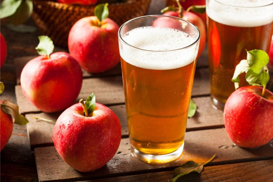 Un vaso de sidra rodeado de manzanas.