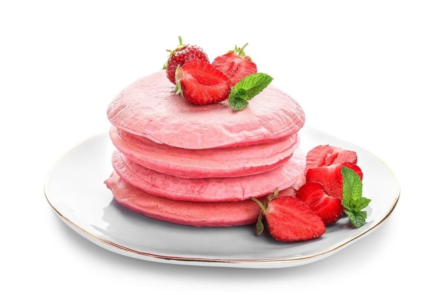 Una pila de tortitas rosadas con fresas.