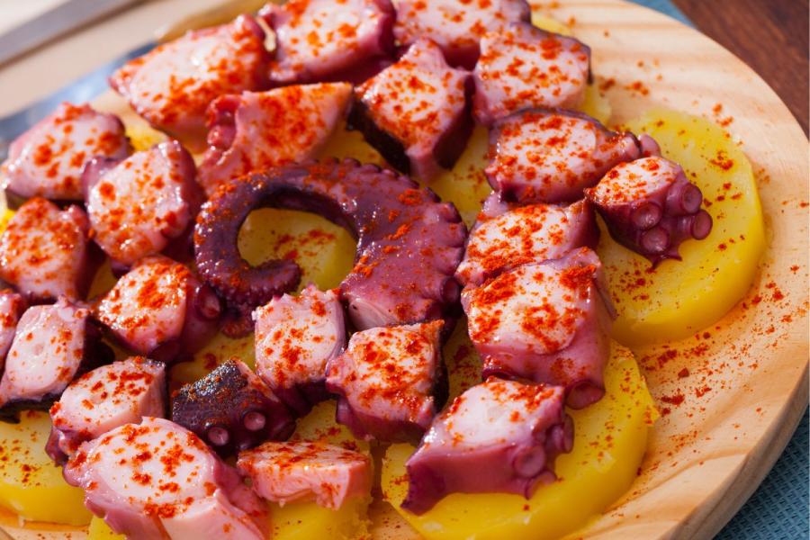 Pulpo a la gallega acompañado de rodajas de patata cocida en plato de madera.