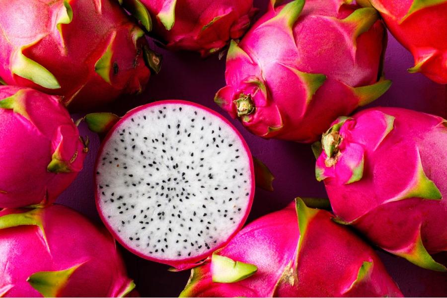 Una pitaya cortada por la mitad transversalmente en medio de varias pitayas enteras.