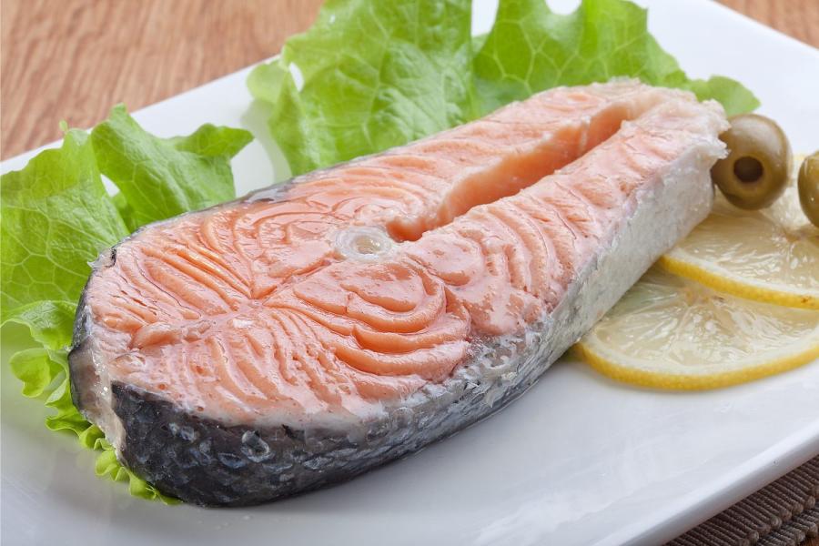 Rodaja de salmón al vapor con rodajas de limón, lechuga y aceitunas.
