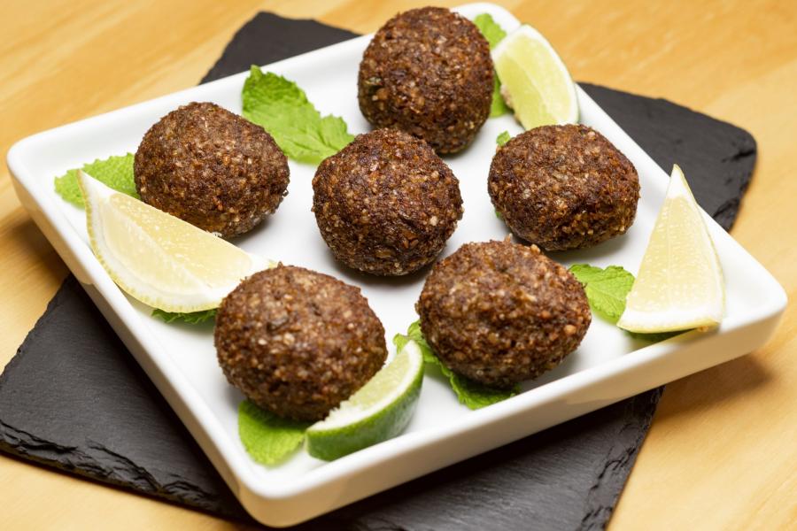 Un plato blanco rectangular con seis bolas redondas de kibbeh fritas, adornadas con rodajas de limón y hojas de menta.