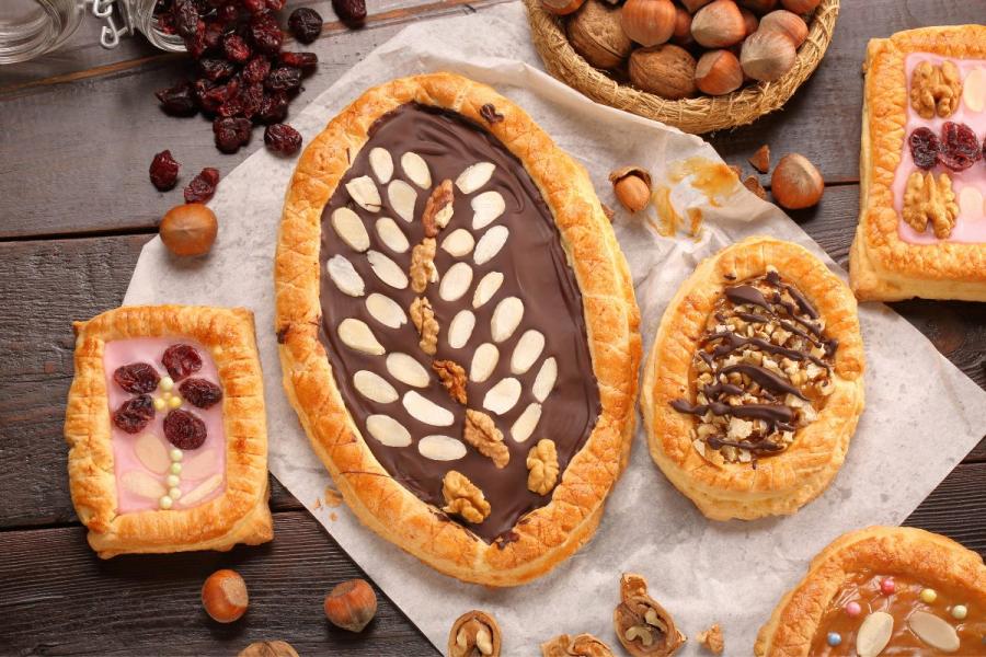 Varios pasteles polacos mazurek decorados con chocolate, nueces y frutas secas, colocados sobre una superficie rústica de madera con avellanas y arándanos secos.