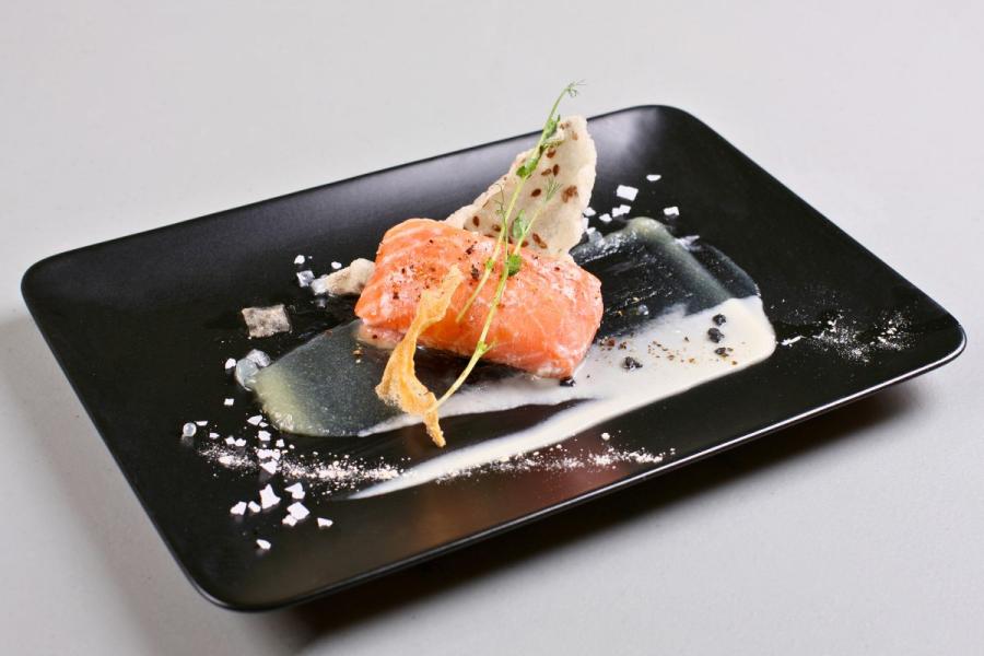 Un plato rectangular de color negro con salmón ahumado y salsa preparados siguiendo la técnica de gastronomía molecular.