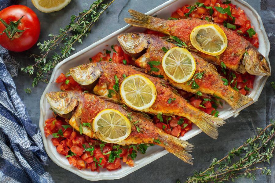 Salmonetes al horno servidos sobre una cama de tomate concasé y decorados con rodajas de limón y hierbas frescas.