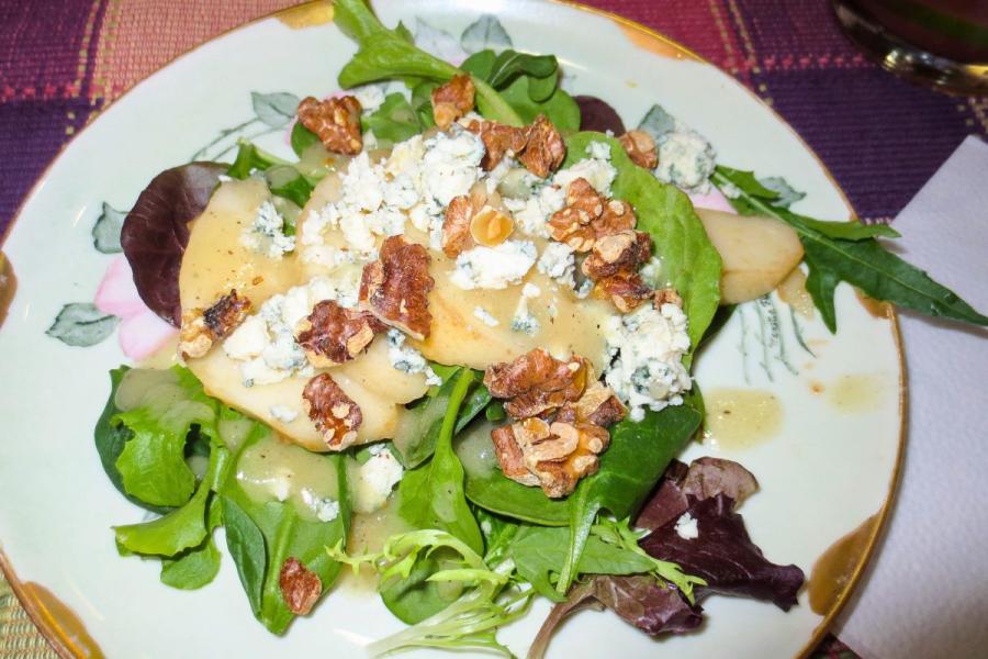 Un plato con ensalada de hojas variadas, queso azul, nueces y pera.