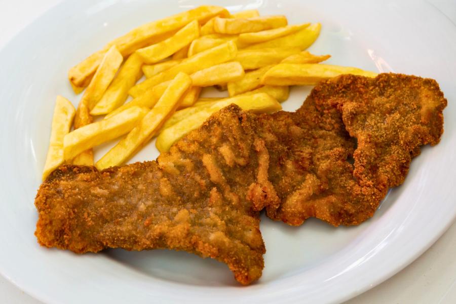 Un plato con un filete empanado y patatas fritas.