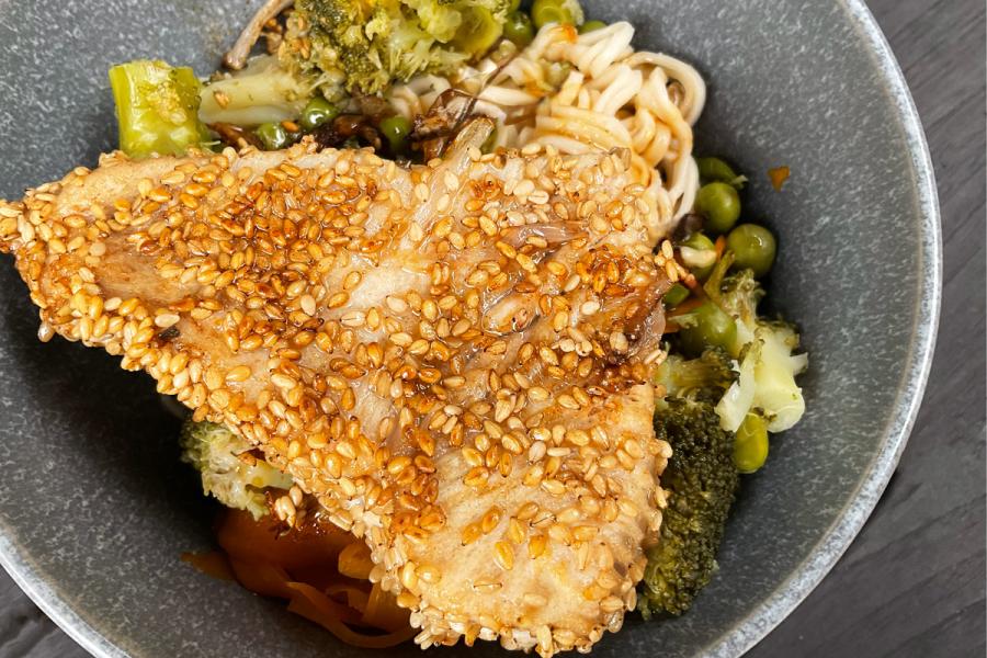 Un cuenco con atún al sésamo servido sobre verduras y fideos chinos.