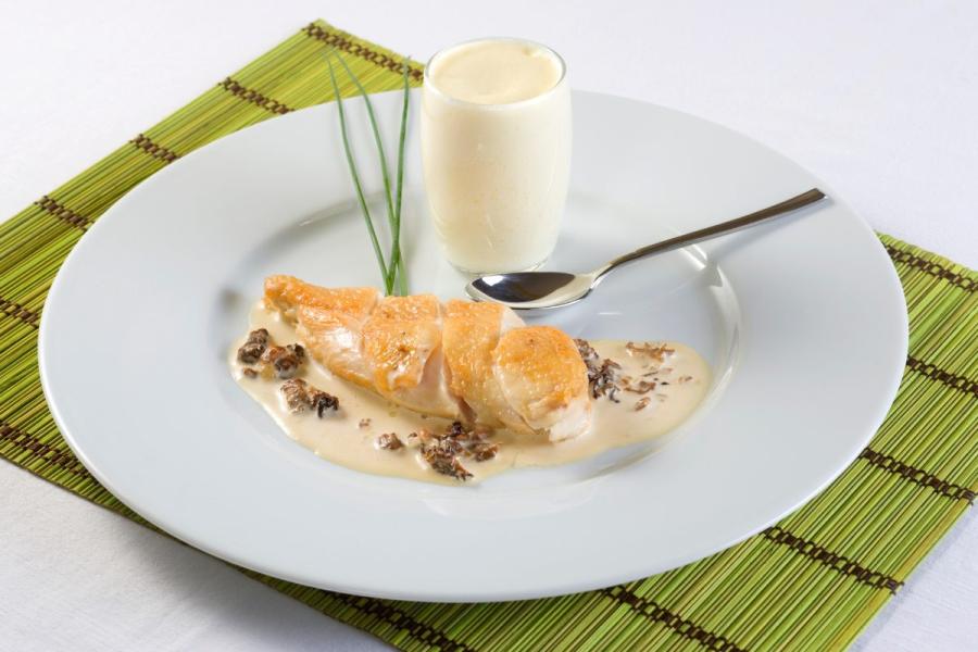 Un plato de pollo suprema con setas picadas acompañado de puré de apio en vaso.
