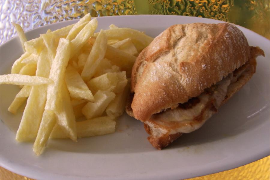 Montadito de lomo de cerdo y patatas fritas con jarras de cerveza al fondo.