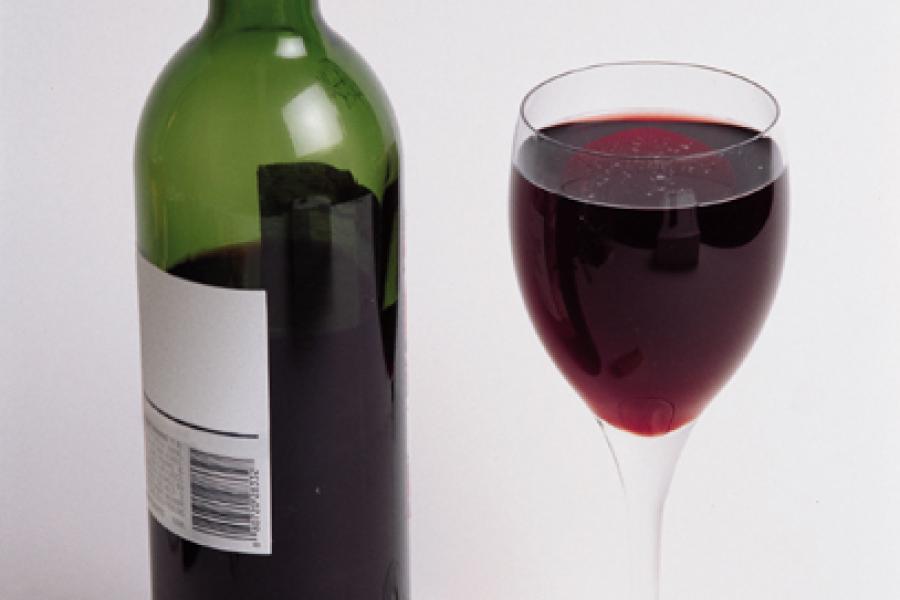 Una botellad de vino tino y una copa con vino tinto.