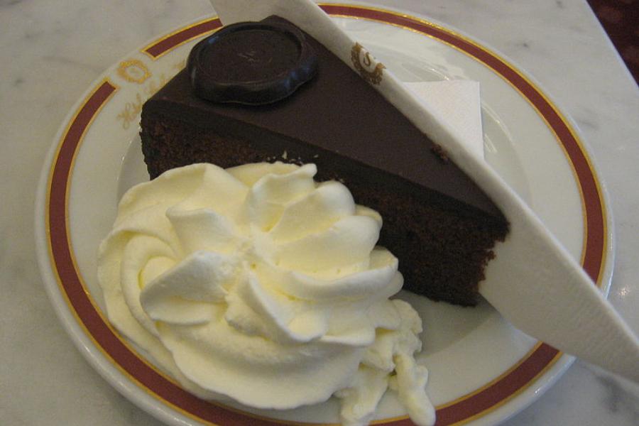 Un trozo de sachertorte en un plato, acompañado de nata montada.