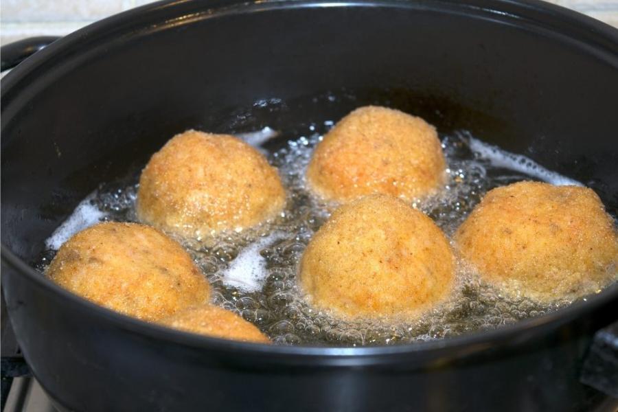 Croquetas de arroz, o arancini, friéndose.