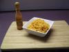 Un recipiento con arroz al estilo mexicano sobre una mesa con una botella de salsa al lado.