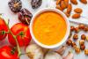 Salsa romesco rodeada de parte de sus ingredientes, tomate, pimiento seco, ajo, almendras y avellanas.