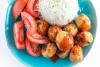Un plato de bolitas de pollo con salsa agridulce acompañadas de arroz hervido y trozos de tomate.