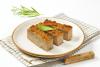 Rodajas de pastel de hígado y carne de cerdo en un plato, acompañadas de hierbas aromáticas.