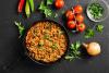 Curry kima en una sartén de hierro rodeado de algunos de sus ingredientes.