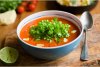 Un cuenco con sopa de jitomate decorada con nata líquida, aceite de oliva y cilantro fresco.
