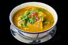 Un cuenco con sopa vietnamita de calabaza contra un fondo negro.